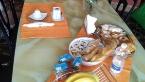 Una mesa de comedor preparada para el desayuno, con pan, plátanos y una botella de agua.
