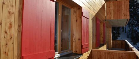 A wooden cabin with red shutters, a balcony, and a window.