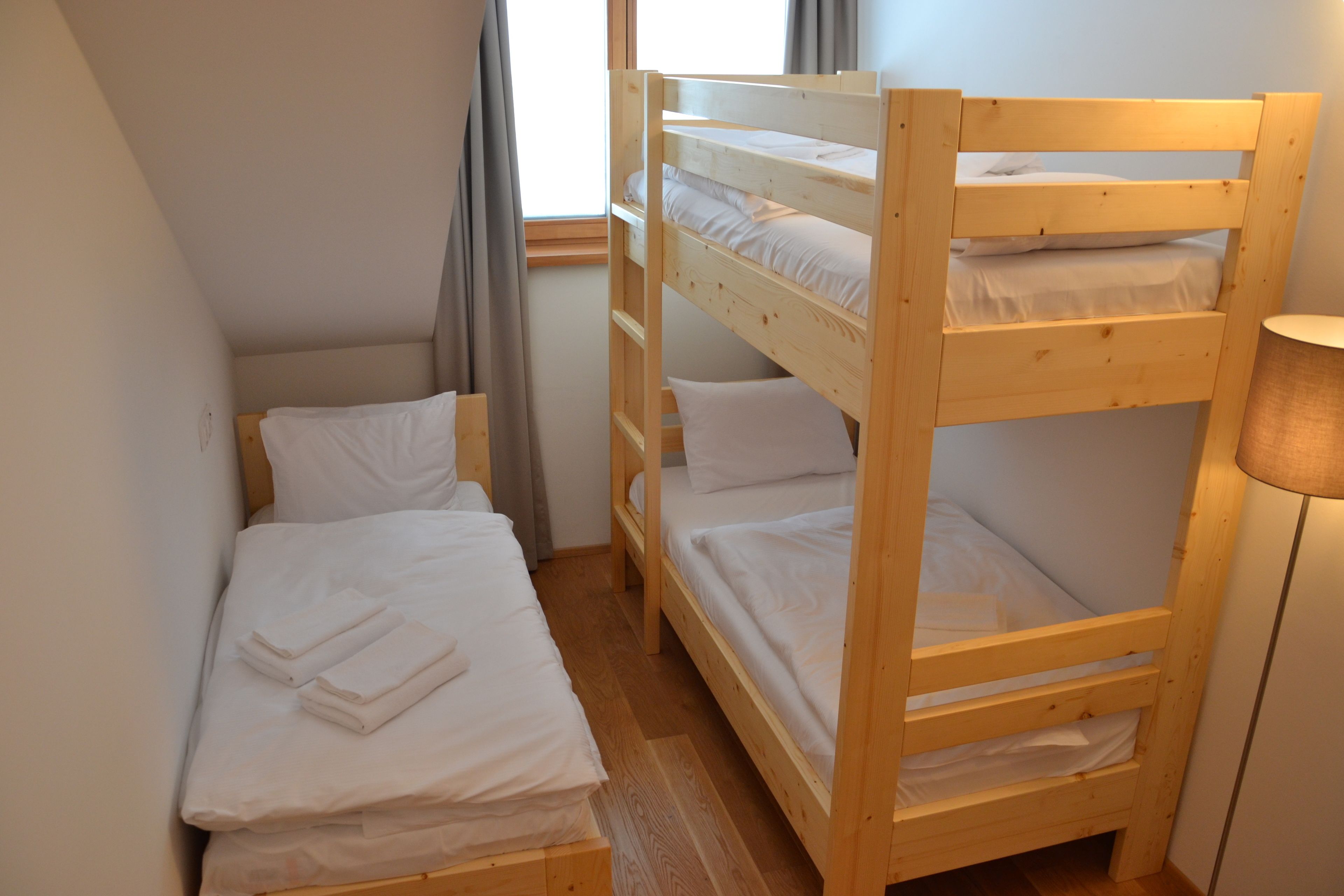 A bunk bed room with white bedding, a lamp, and a window with curtains.