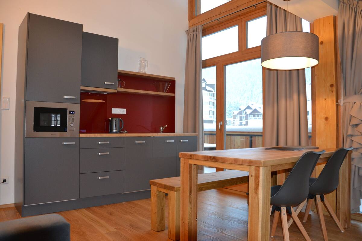 A compact kitchen with grey cabinets, a wooden dining table, and two black chairs.