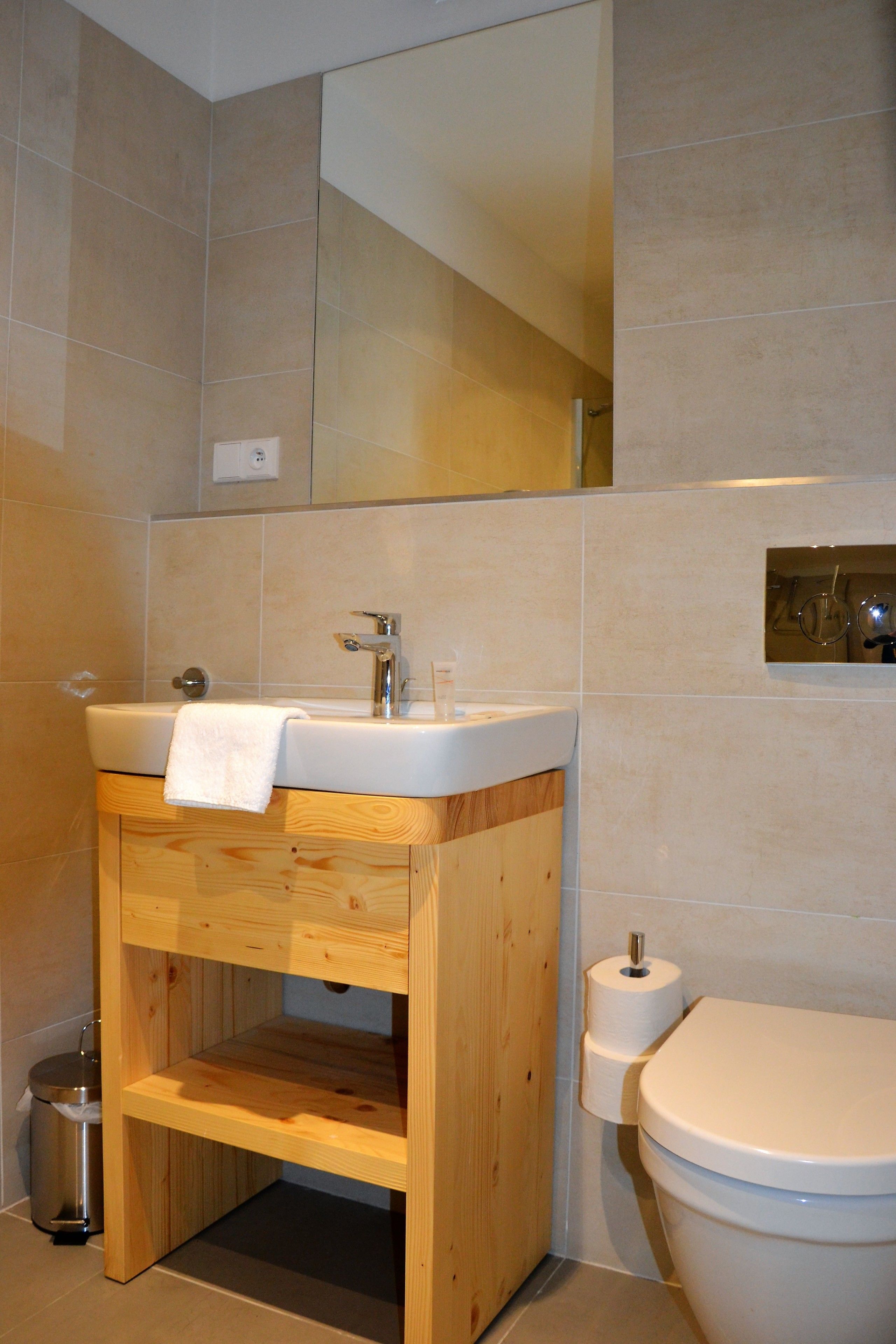 Un baño con tocador de madera, lavamanos, espejo, inodoro y cubo de basura.