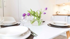 Una mesa de comedor dispuesta con platos blancos, cubiertos y un tazón de vidrio transparente con tulipanes morados.