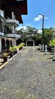 Un edificio con un camino de grava que conduce a un mirador, rodeado de plantas en macetas y palmeras.