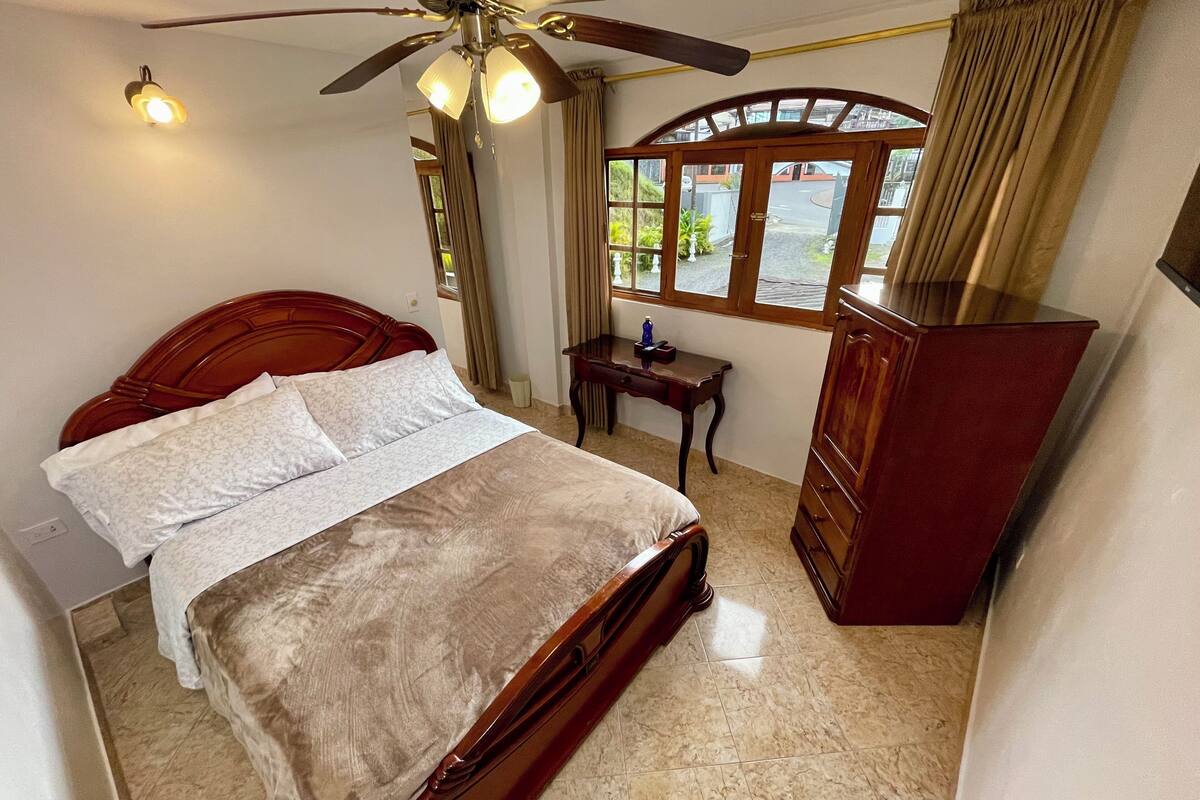 Ein Schlafzimmer mit einem Holzbett, einem Schreibtisch, einem Kleiderschrank und einem Deckenventilator.