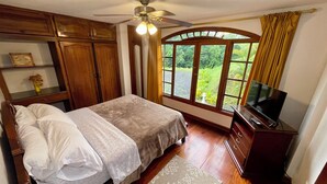 Une chambre à coucher avec un lit, un ventilateur de plafond, une télévision et une fenêtre avec des rideaux.