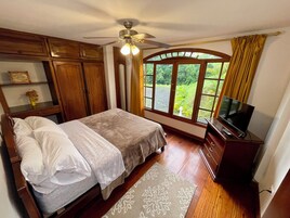 Un dormitorio con cama, ventilador de techo, televisor y ventana con cortinas.