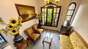Un salon comprenant un canapé, deux fauteuils, une table basse, un tableau, un vase avec des tournesols et une fenêtre donnant sur un paysage verdoyant.