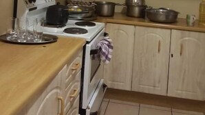 A kitchen with light wooden cabinets, a stove, and various pots and pans. - Premier Guest Lodge (Harare)