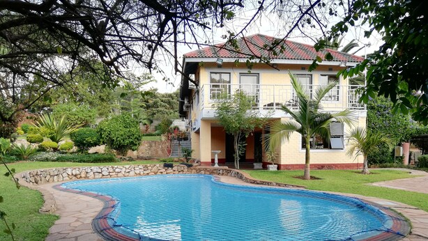 A swimming pool with a stone border, surrounded by a well-maintained lawn and various plants. - Premier Guest Lodge (Harare)