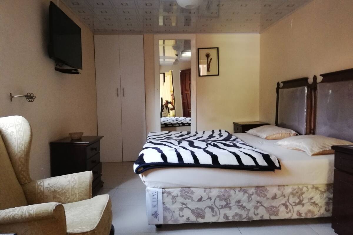 A bedroom with a bed, a chair, a dresser, a television, and a door leading to another room.