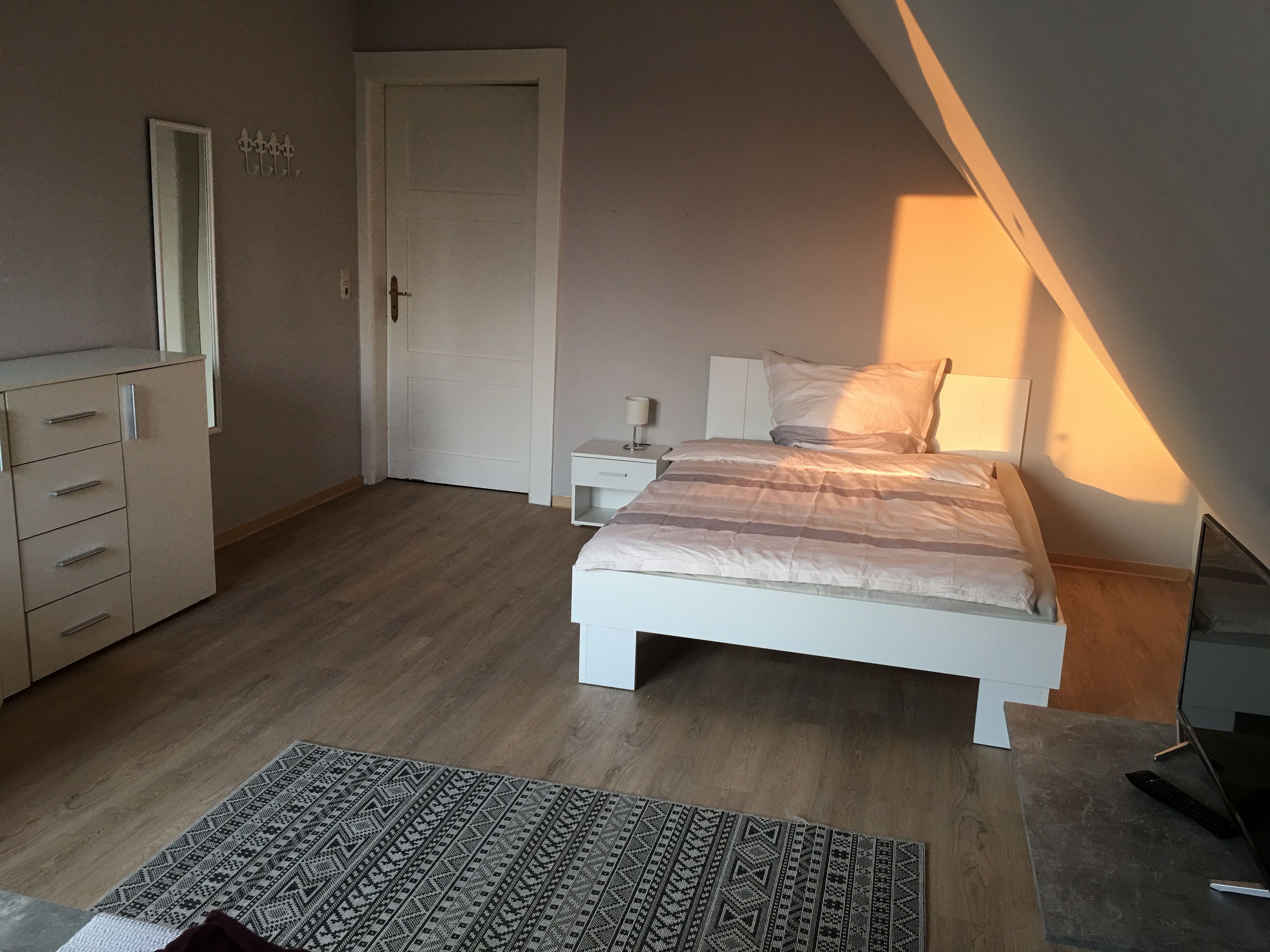 Een slaapkamer met een bed, nachtkastjes, een dressoir, een spiegel en een tapijt met een patroon.