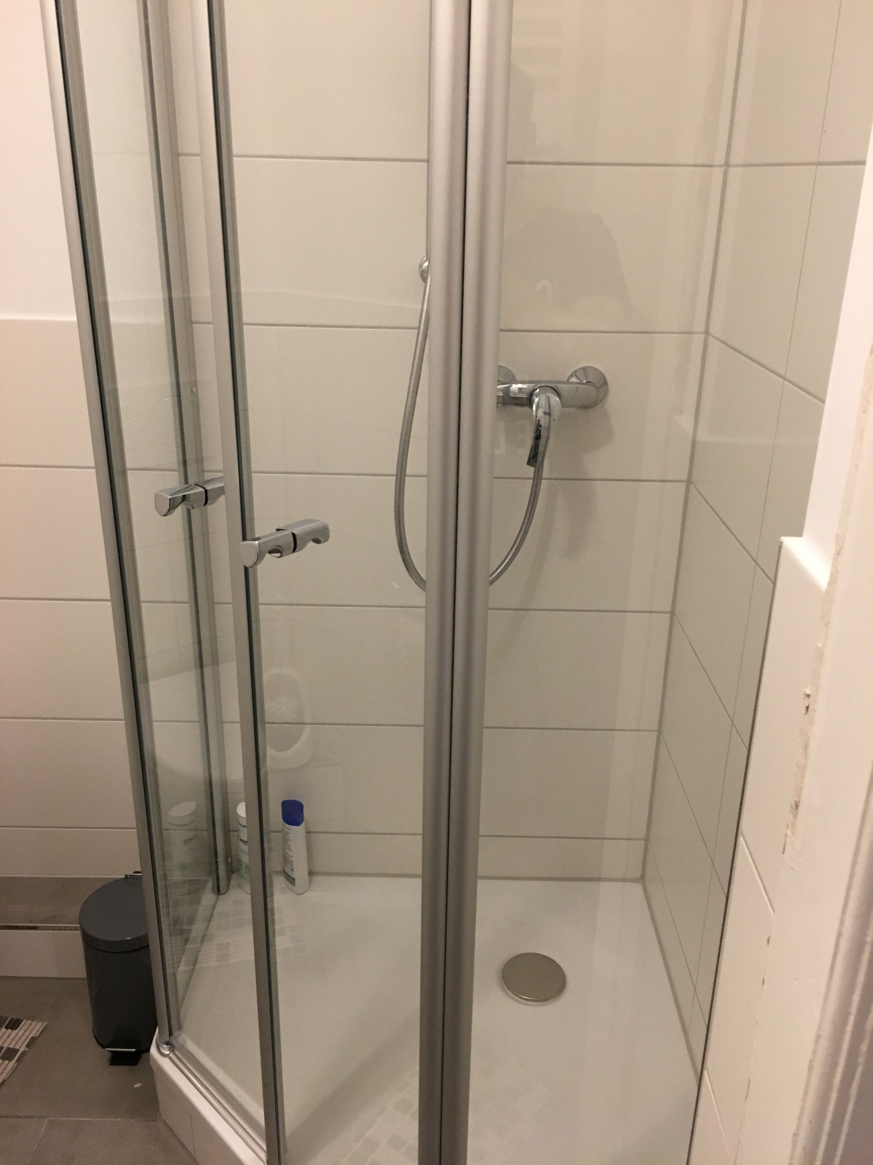 A glass-enclosed shower with a handheld showerhead and a wall-mounted faucet.