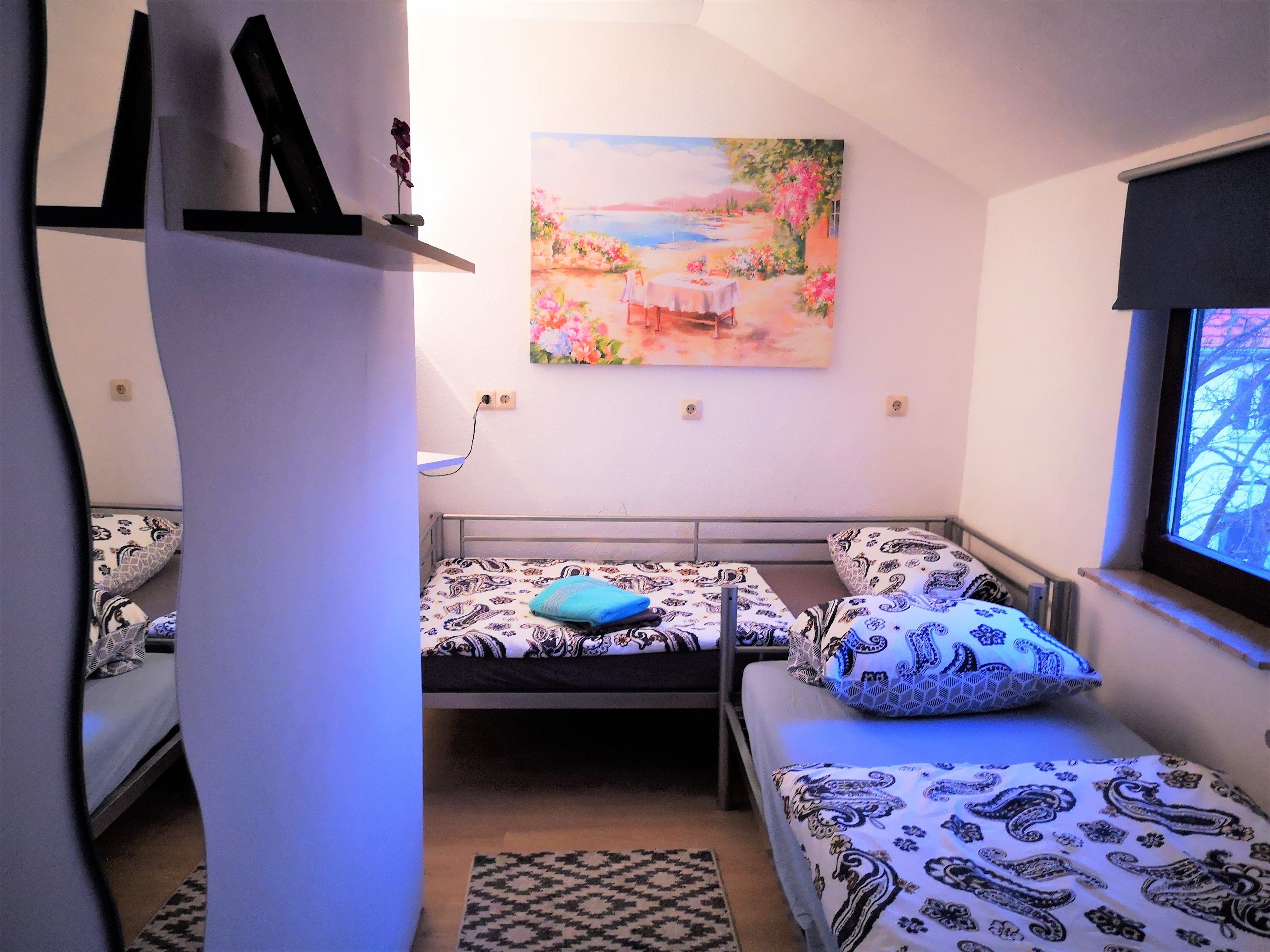 A room with two beds, a painting on the wall, and a window with a view.