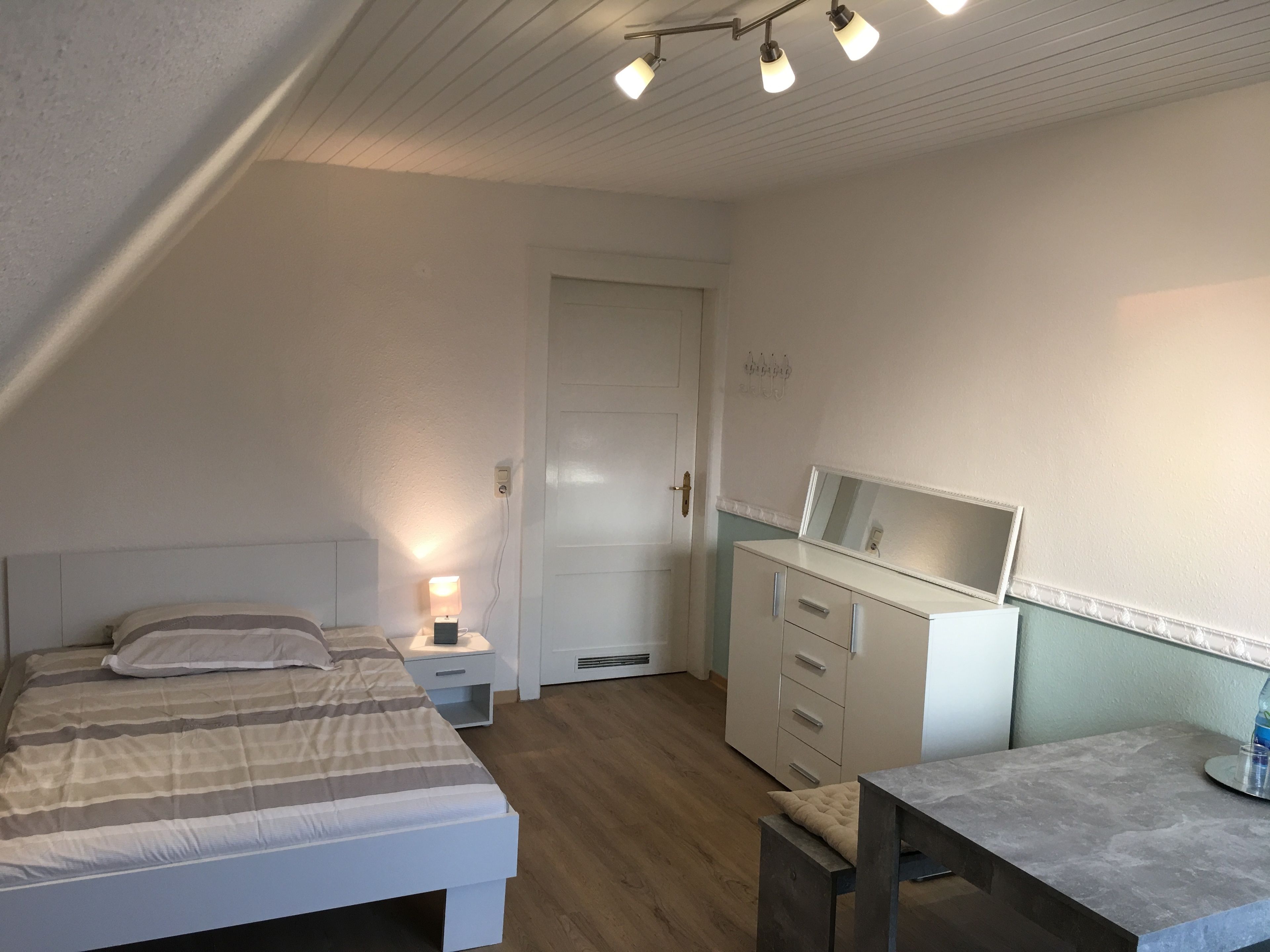 Quarto com cama, mesa de cabeceira, cômoda e escrivaninha com cadeira.