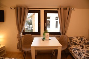 A room with a window, a table with a bottle and a card, two chairs, and a bed with patterned bedding. - Gästeliesel Göttingen (Goettingen)