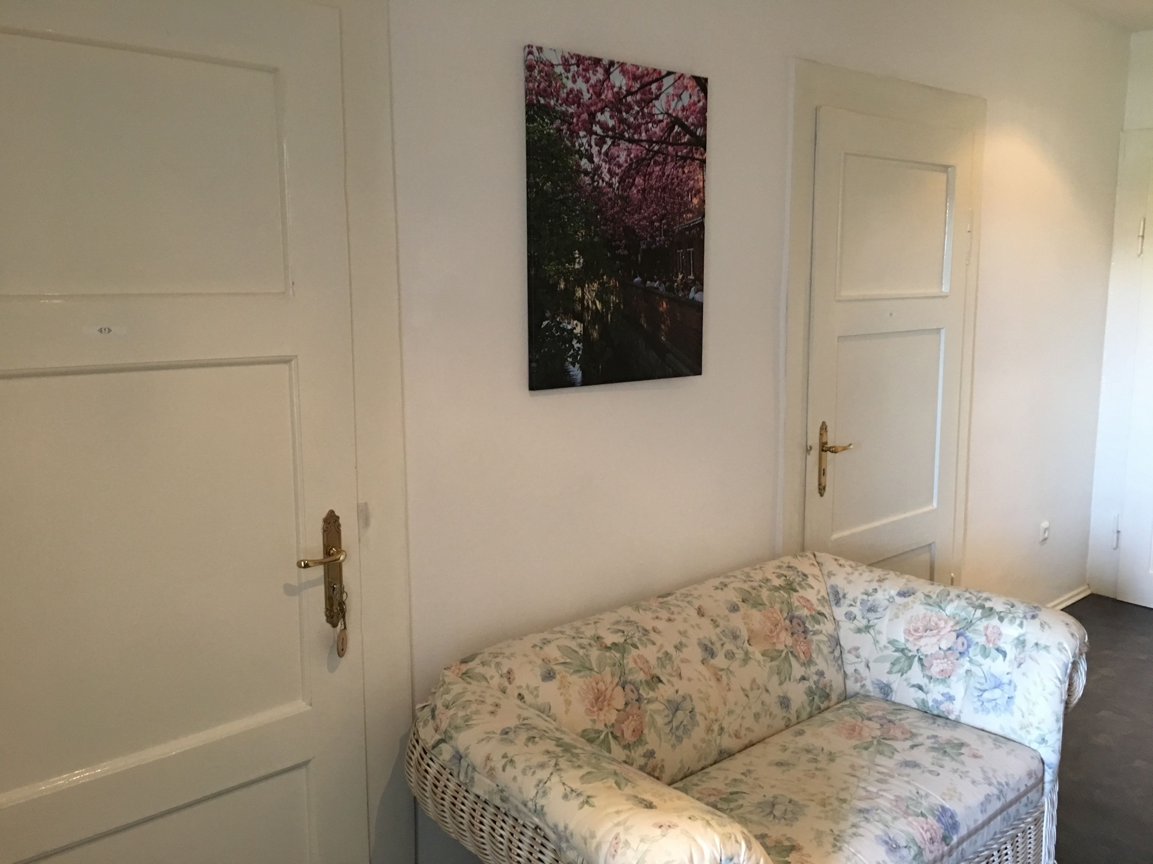 A room with two white doors, a floral sofa, and a painting of cherry blossoms on the wall.
