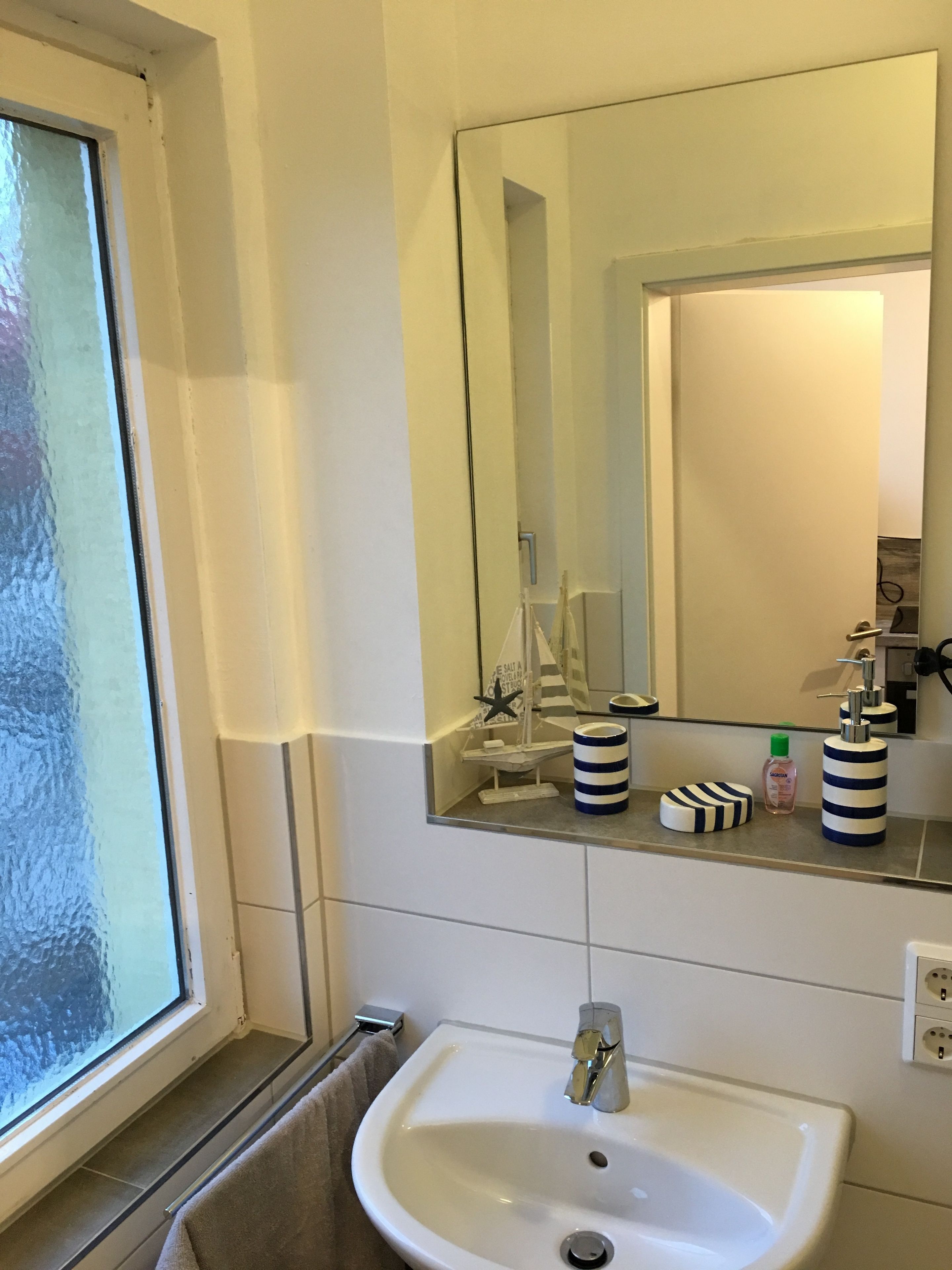 A bathroom with a white sink, a mirror, and a window.