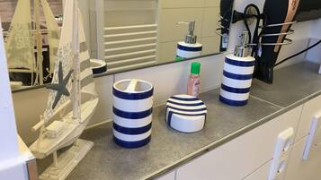 Une salle de bain avec un grand miroir, des distributeurs de savon à rayures, un porte-brosse à dents et une maquette de bateau décorative.