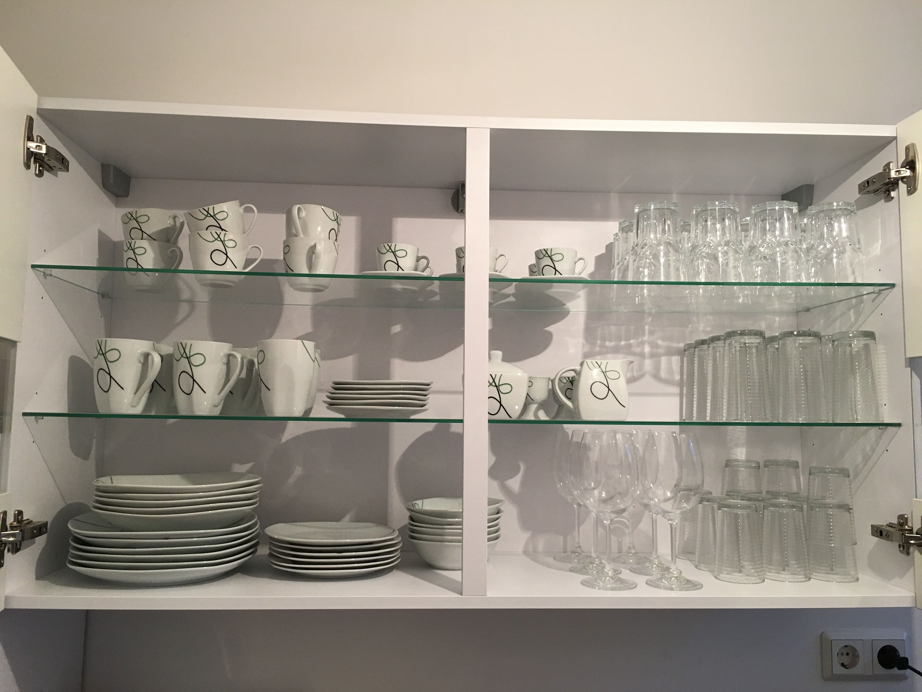 A display of white ceramic mugs, plates, and clear glassware on glass shelves.