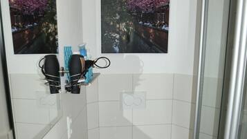 A bathroom with a white sink, a toilet, and a glass shower enclosure. There are two framed pictures on the wall above the sink.