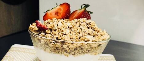 Een dessert in een glazen schaal met een laagjesstructuur, afgetopt met granola en aardbeien.