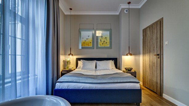 Een slaapkamer met een groot bed, een houten garderobe en twee kunstwerken in lijsten aan de muur.