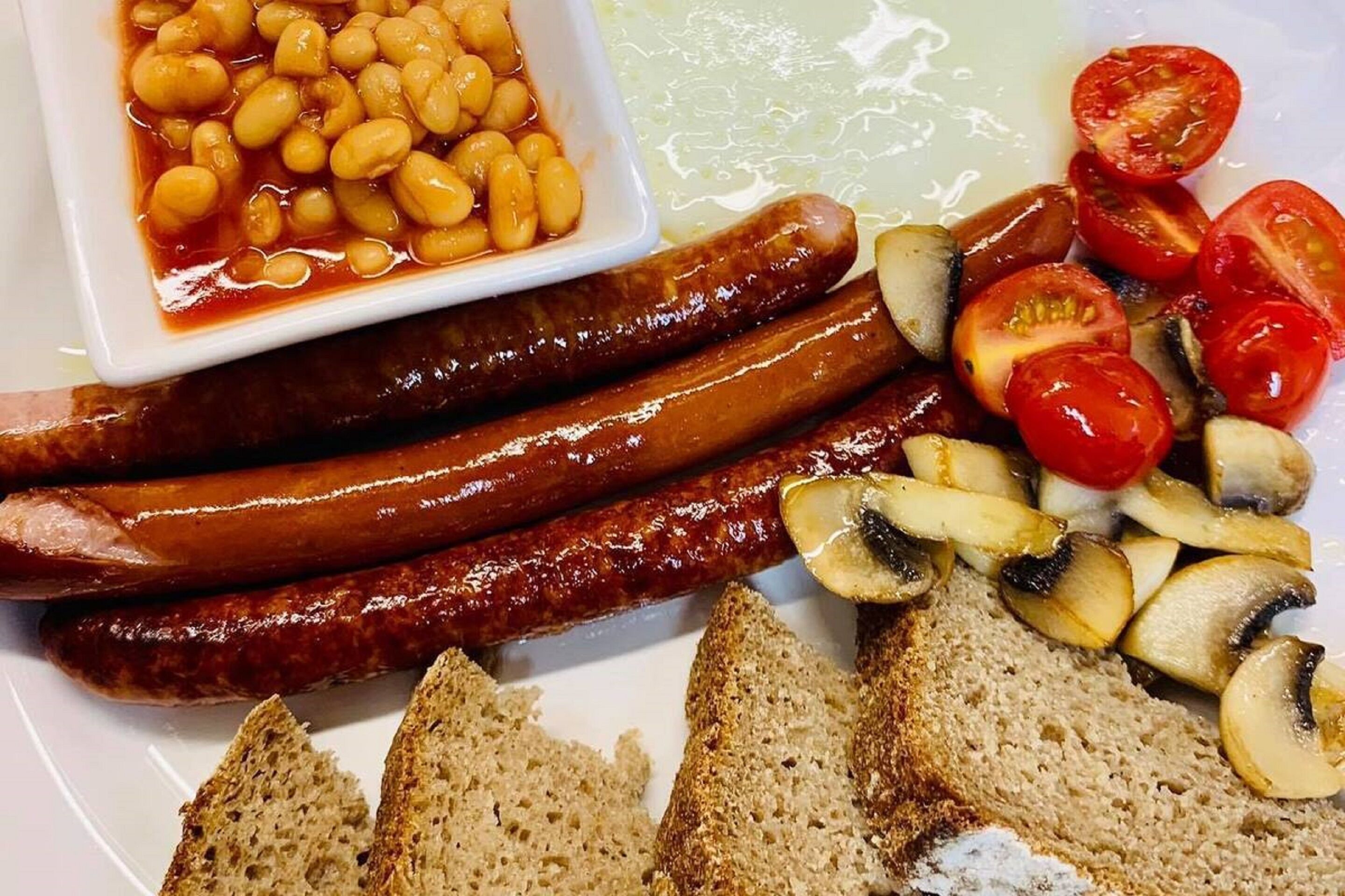 Une assiette garnie de saucisses, de tomates en tranches, de champignons et de pain grillé.