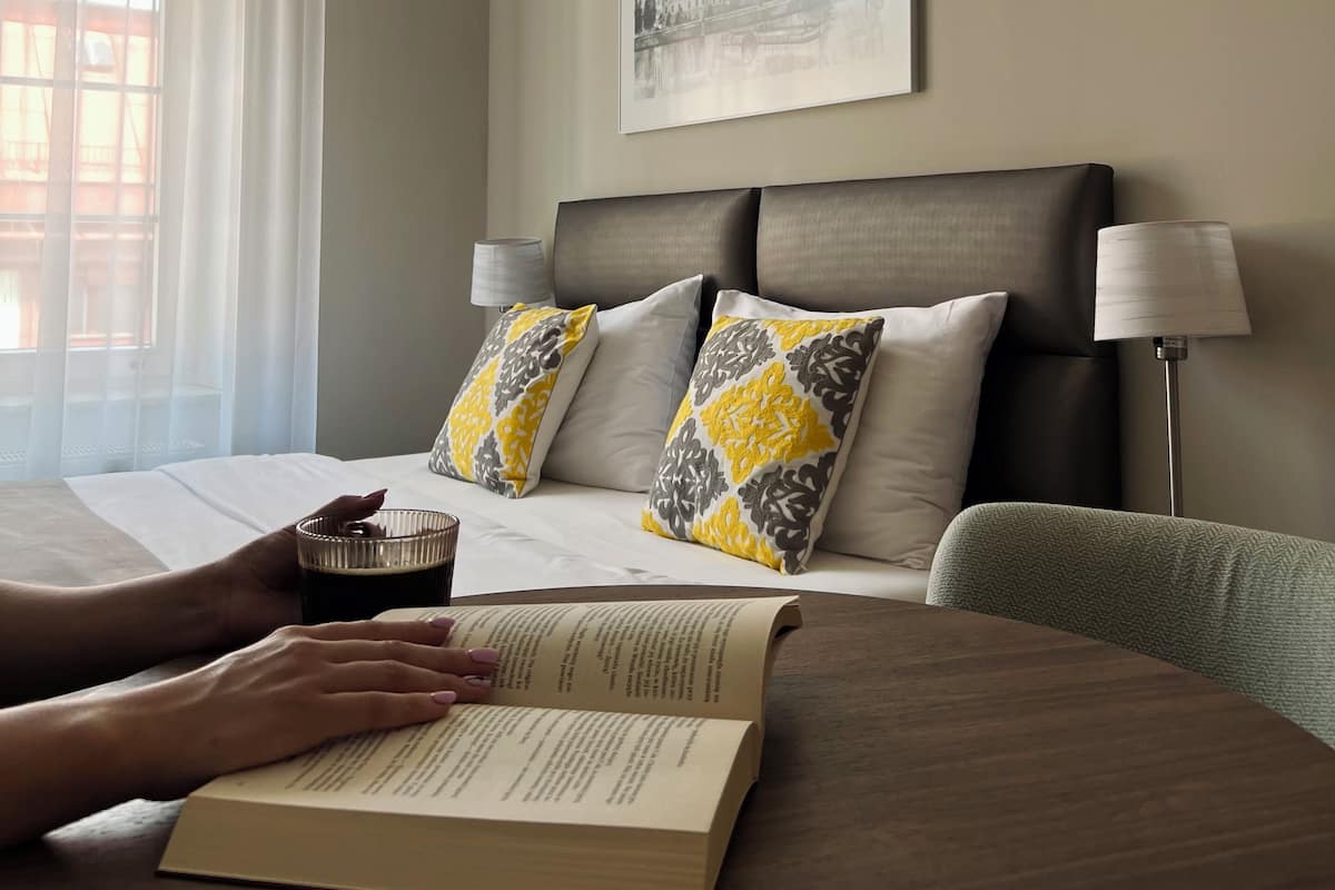 Een hotelkamer met een bed, een nachtkastje met een boek, een lamp en een schilderij aan de muur.
