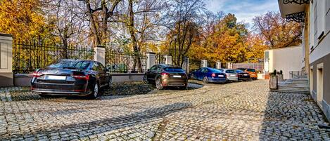 Un camino de adoquines que lleva a una entrada porticada con coches estacionados.