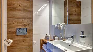 A modern bathroom with a wooden accent wall, a white toilet, a glass-enclosed sink, and a mirror.