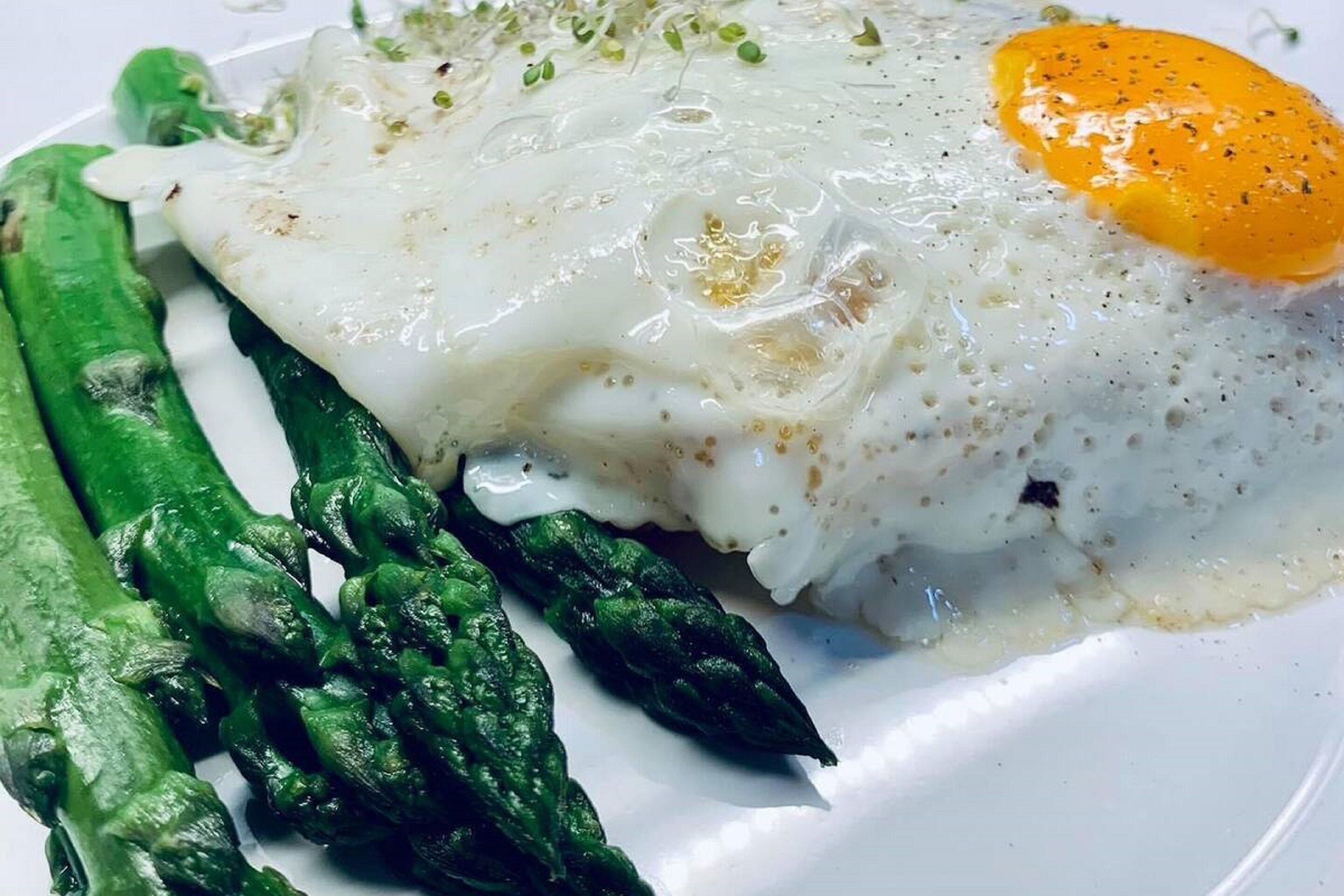 A plate with a fried egg, asparagus, and a creamy sauce.
