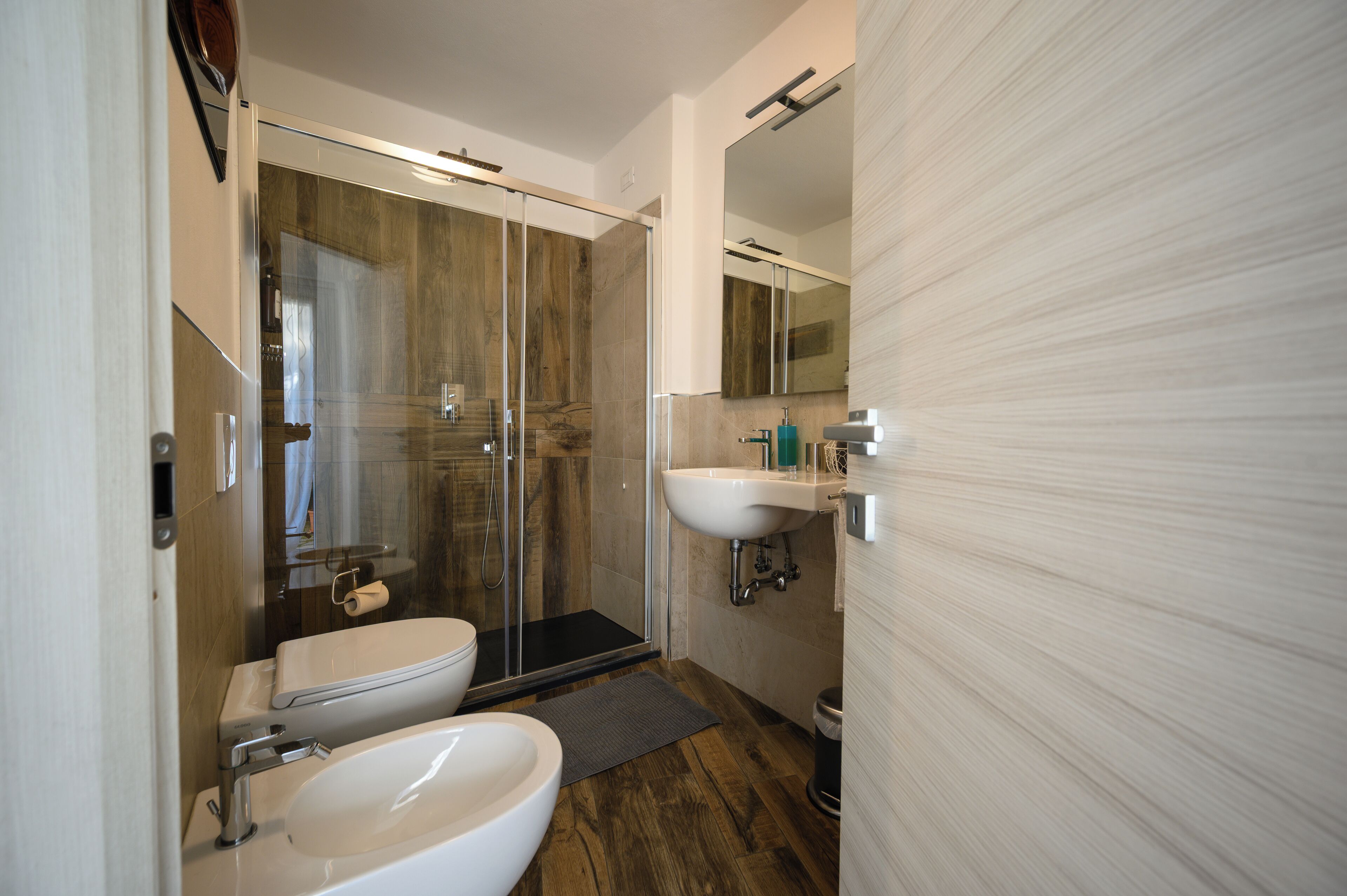 Een moderne badkamer met een douchecabine van glas, een wit wastafeltje en een toilet.