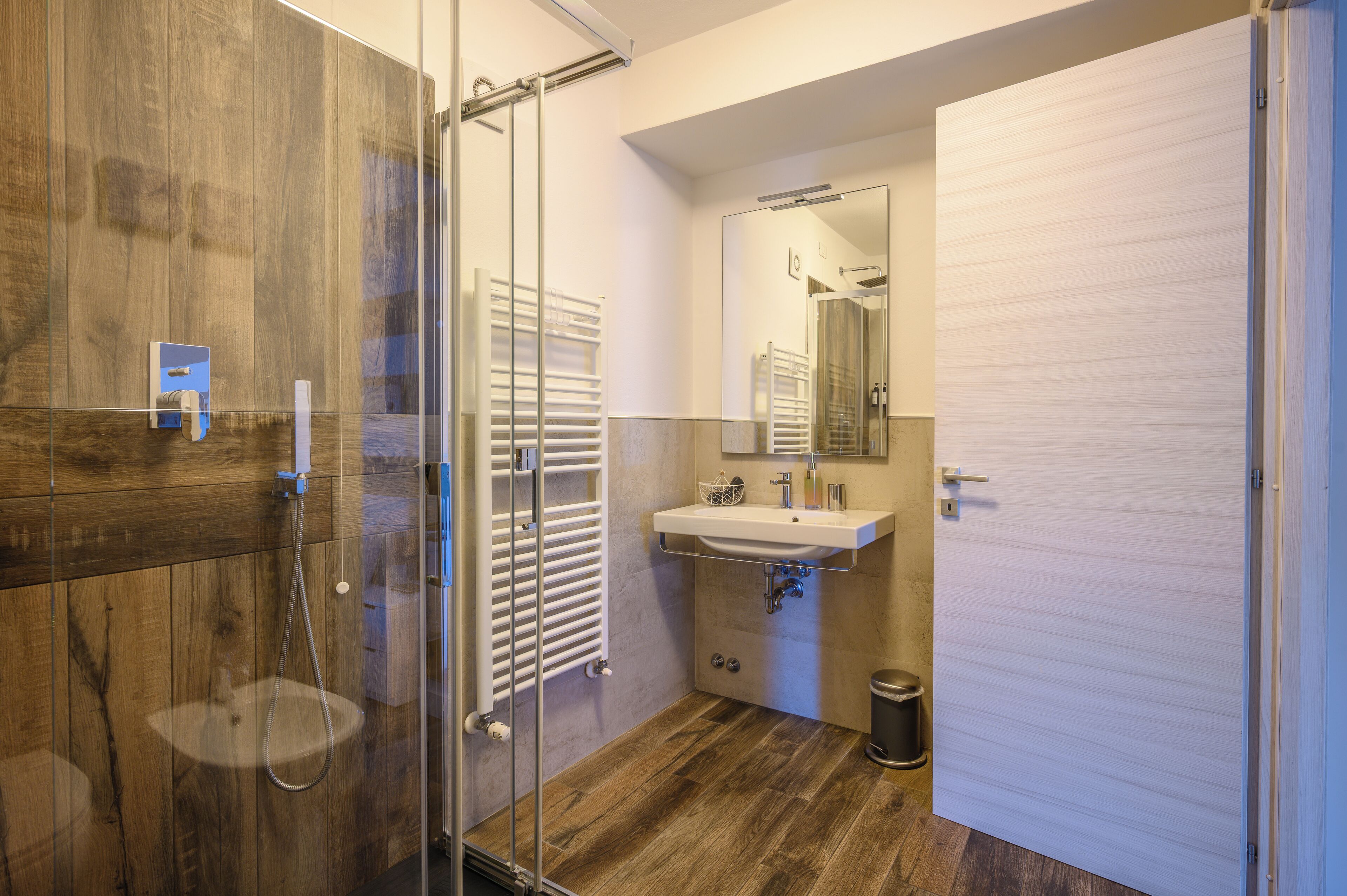 A bathroom with a glass shower enclosure, a wooden vanity, a sink, and a mirror.