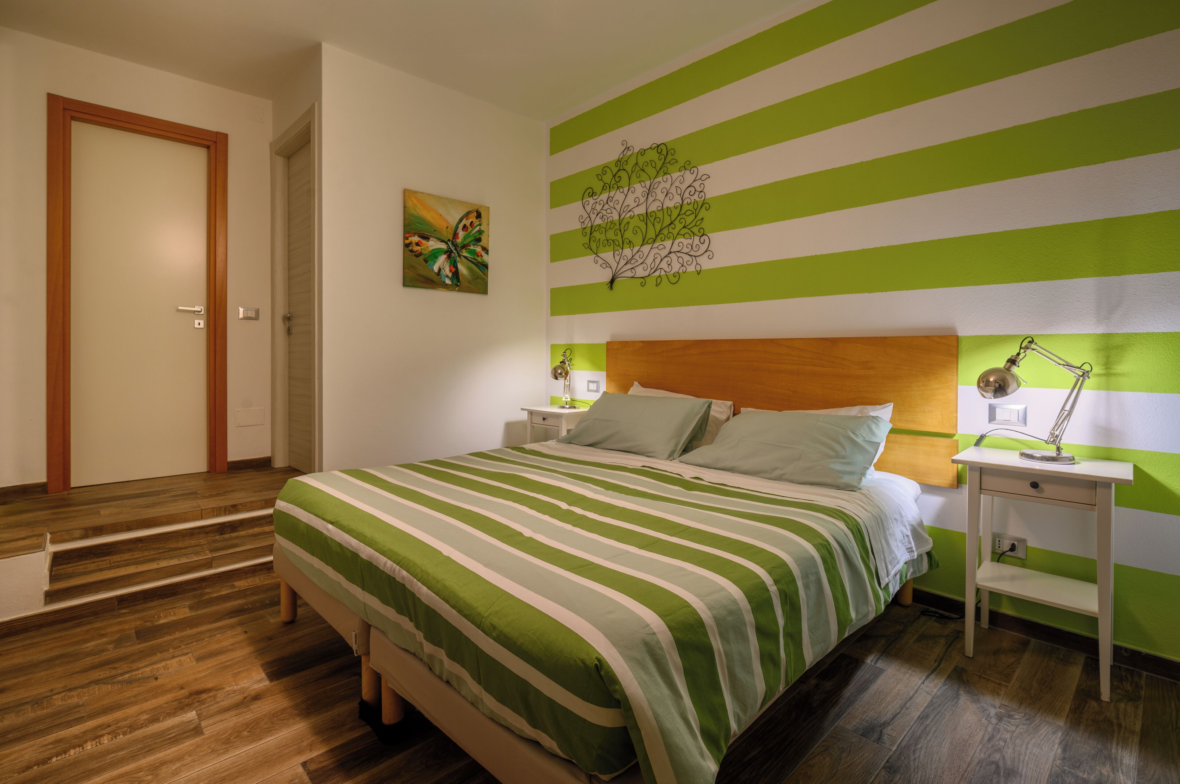Une chambre à coucher avec un lit, des tables de chevet, une lampe, un tableau et une porte.
