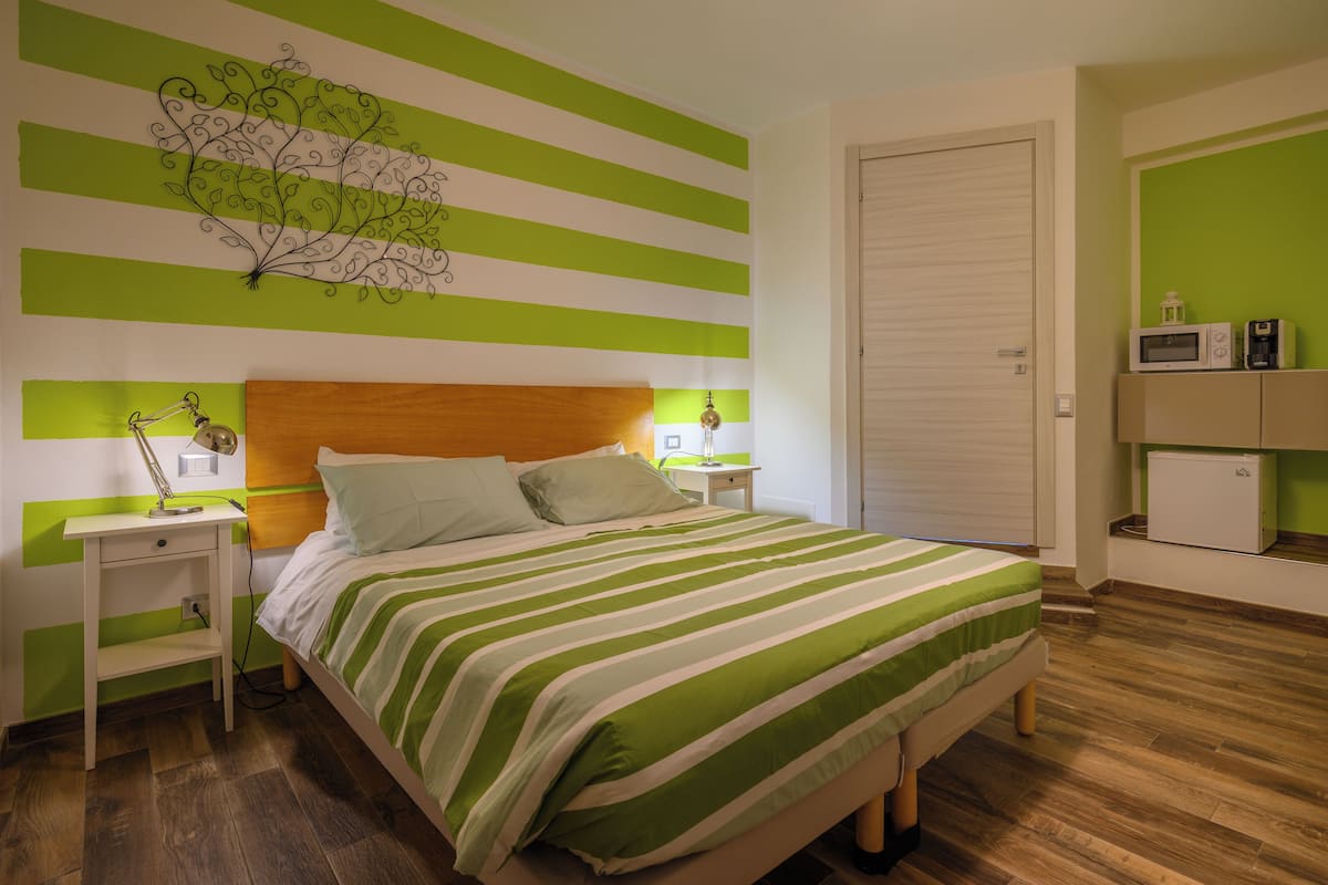 Un dormitorio con cama, mesitas de noche, cómoda y pared con rayas verdes.