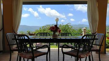 A table with four chairs and a vase of flowers, set on a terrace with a view of mountains and a clear sky.