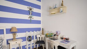 A room with a striped blue and white wall, a white desk with a chair, a small bedside table with a lamp, and a shelf with decorative items. - Il Murice B&B (Vezzano Ligure)