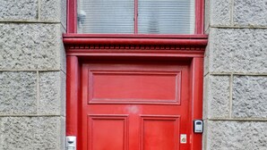 A red door with a brass handle and a mail slot, set in a stone wall. - Modern Central Apartment (Aberdeen)