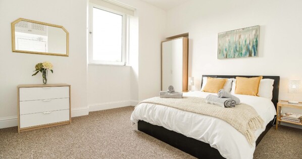 A bedroom with a bed, a dresser, a mirror, a window, and a painting on the wall. - Modern Central Apartment (Aberdeen)