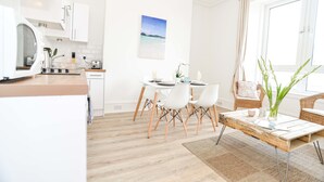 A modern kitchen with white cabinets, a wooden countertop, and a dining area with white chairs and a table. - Modern Central Apartment (Aberdeen)