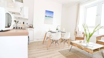 A modern kitchen with white cabinets, a wooden countertop, and a dining area with white chairs and a table.
