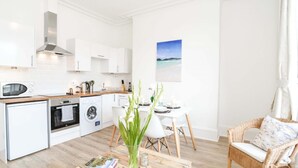 A modern kitchen with white cabinetry, a microwave, a coffee maker, and a dining area with a table and chairs. - Modern Central Apartment (Aberdeen)