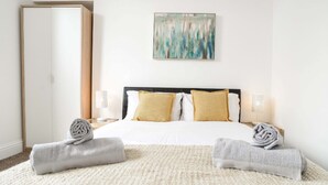 A hotel room with a bed, two bedside lamps, a painting on the wall, and two rolled towels on the floor. - Modern Central Apartment (Aberdeen)