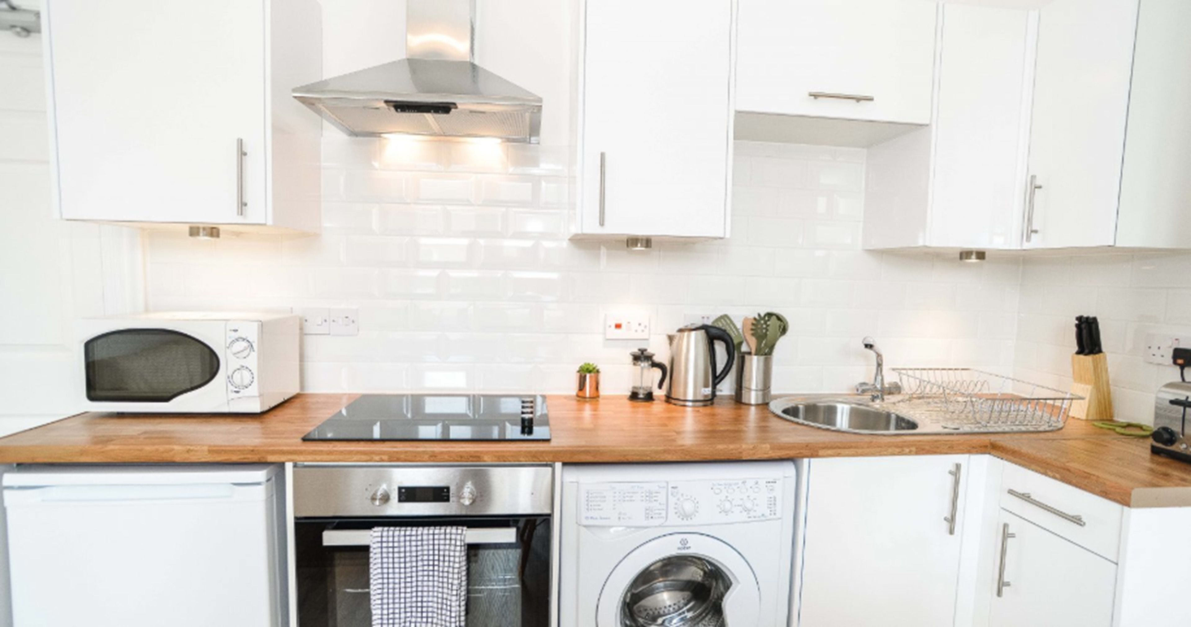 A modern kitchen with white cabinets, stainless steel appliances, a wooden countertop, and a built-in washing machine.
