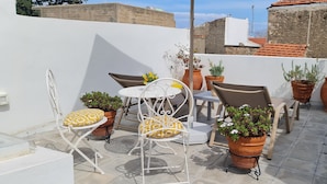 Eine Dachterrasse mit weißen Metallstühlen und -tischen, umgeben von Terrakottatöpfen mit Pflanzen.