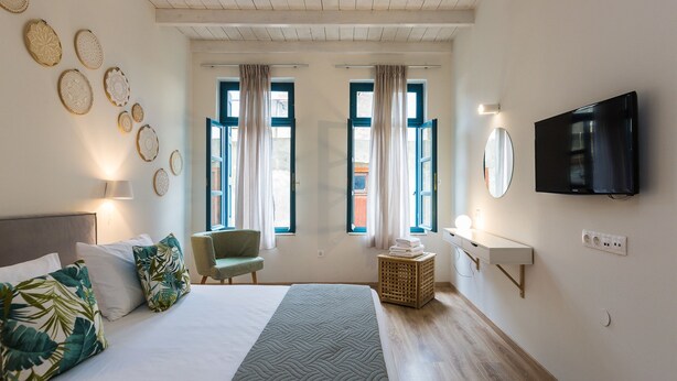 Ein Hotelzimmer mit einem Bett, einem Sessel, einem Fernseher und einem an der Wand befestigten Fernseher.