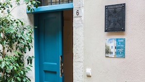 Eine blaue Tür mit der Nummer 6 darüber, ein Blumentopf links und ein an der Wand befestigtes Schild rechts.