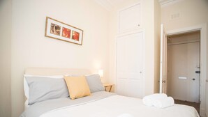 A neatly made bed with pillows and a blanket, a bedside table with a lamp, and a door to the right.