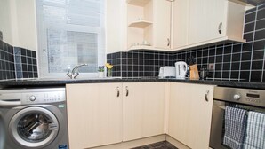 A compact kitchen with a washing machine, oven, and a window with blinds.