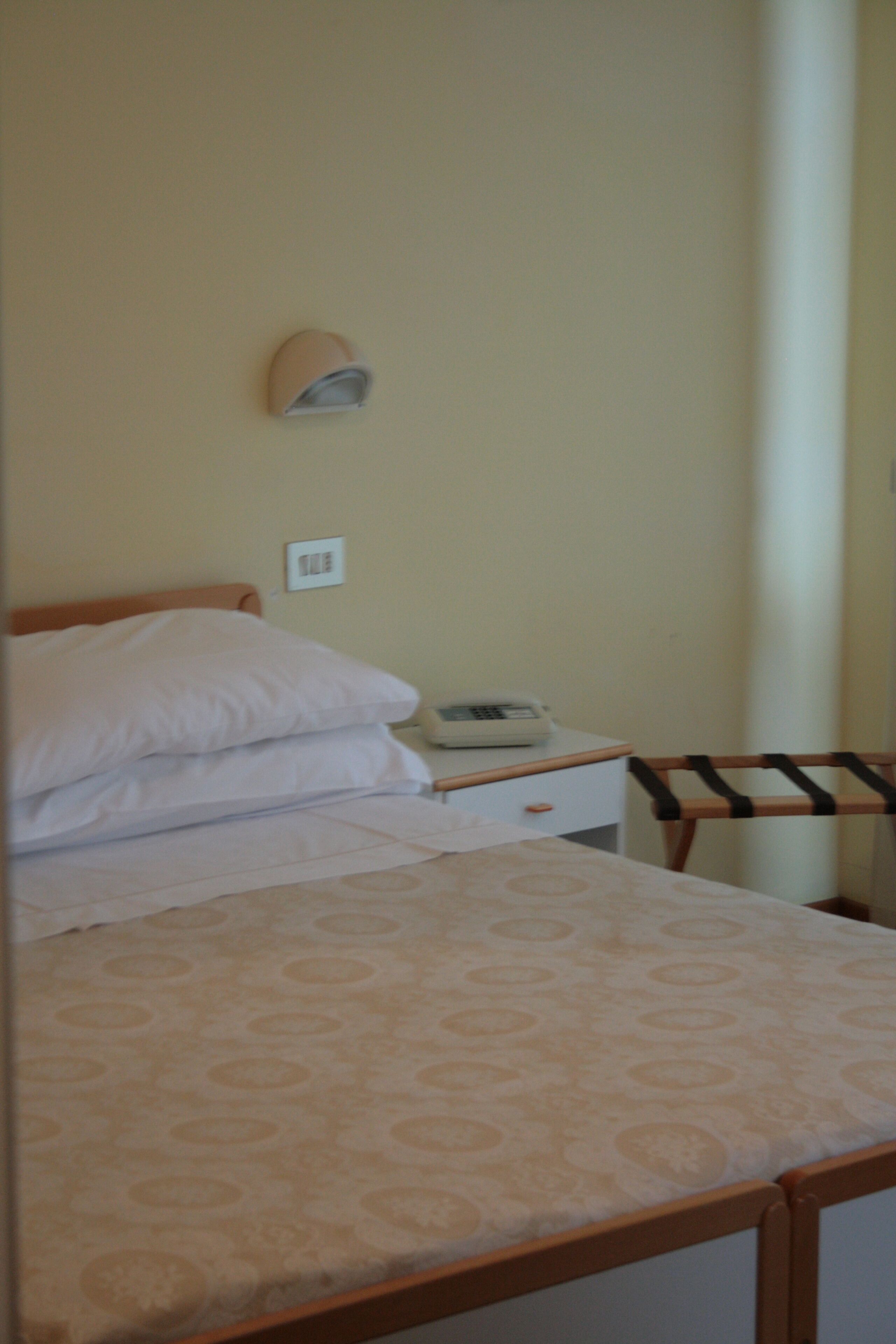 A bed with a patterned bedspread, a bedside table with a phone, and a chair with a wooden frame.